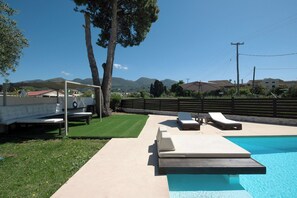Une piscine avec des chaises longues, une pelouse et une vue sur les montagnes.