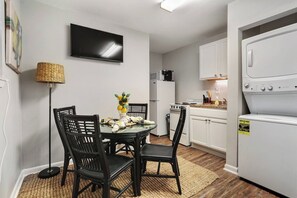 A compact kitchen with white cabinets, a dining table with chairs, a flat-screen TV, and a microwave. - Serenity's Sanctuary| 1BR Near Bourbon & Frenchmen St (New Orleans)