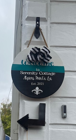A circular sign with a black and white bow, welcoming visitors to Serenity Cottage in Algiers, Pointe La, established in 2021. - Serenity's Sanctuary| 1BR Near Bourbon & Frenchmen St (New Orleans)