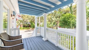 A covered porch with white railings and a blue ceiling, overlooking a lush garden with various trees and a pathway.