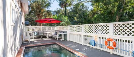 A pool area with a white fence, a red umbrella, and a life preserver.