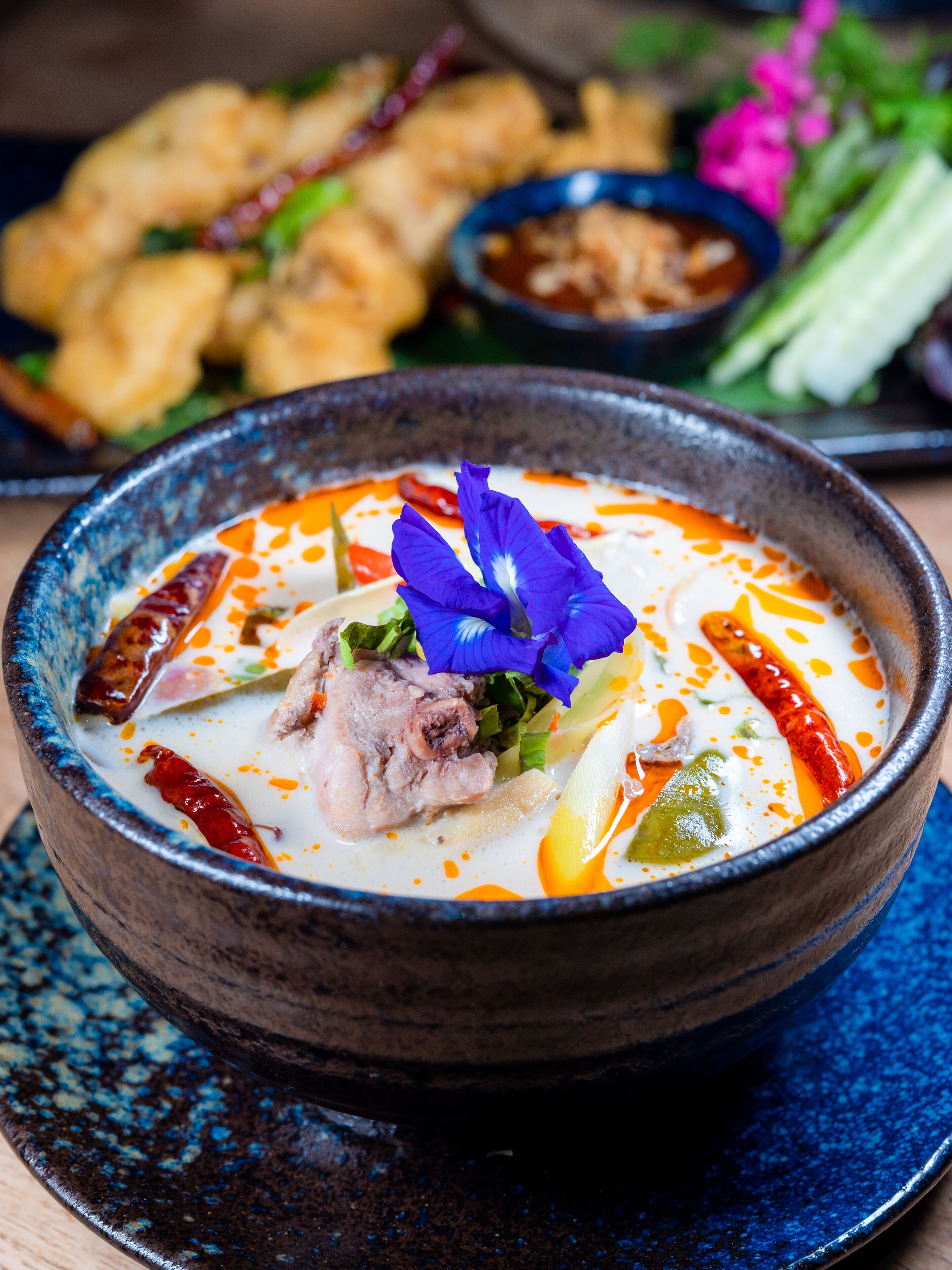 A bowl of soup with meat and vegetables, garnished with a flower, on a blue plate.