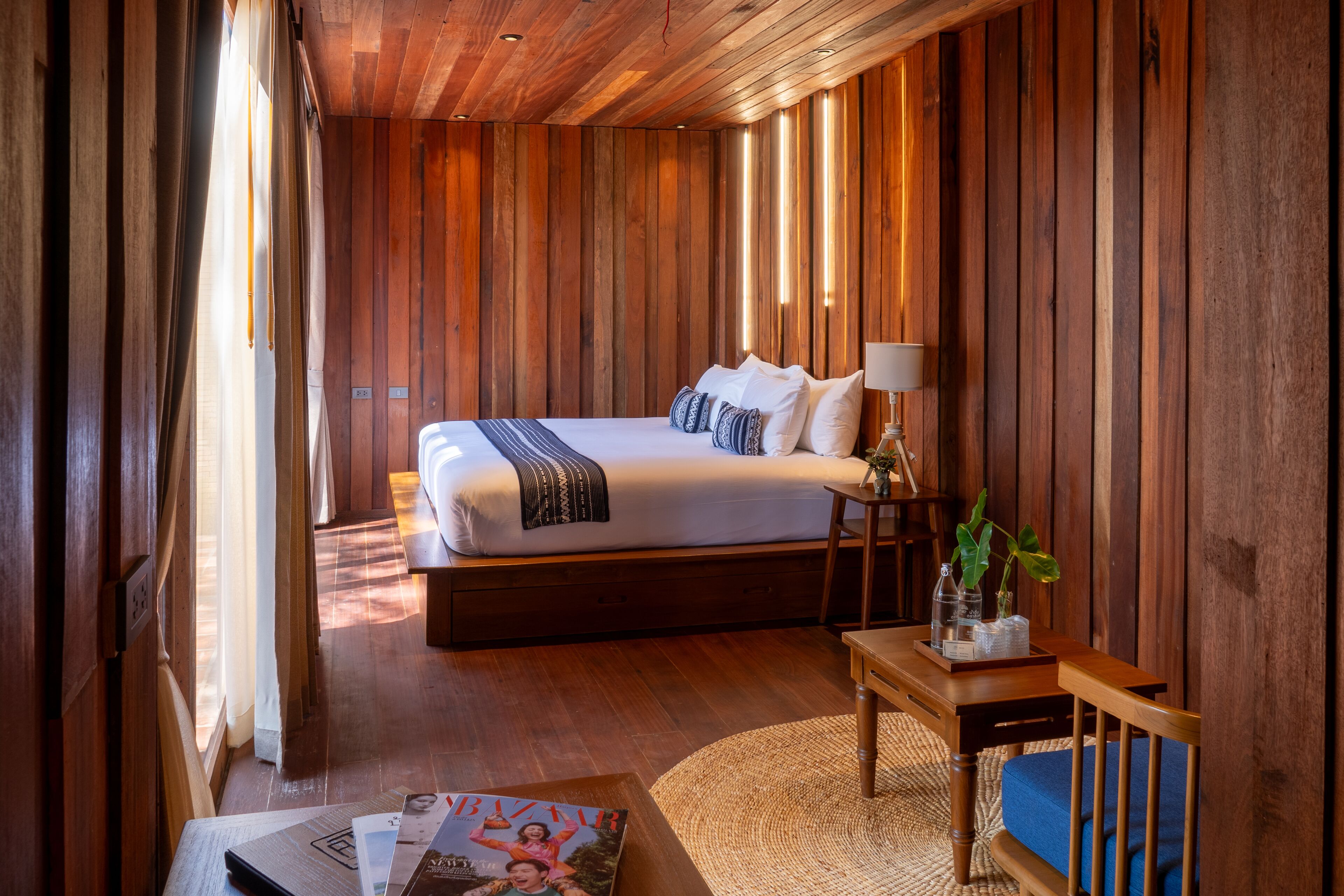 A bedroom with a large bed, bedside table, lamp, and a small plant.
