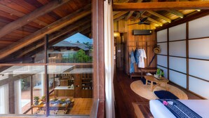 Ein geräumiges Zimmer mit hohen Decken, Holzbalken, einer Glastür zum Außenbereich, einer kleinen Sitzecke mit Tisch und Stühlen und einer traditionellen japanischen Schiebetür.