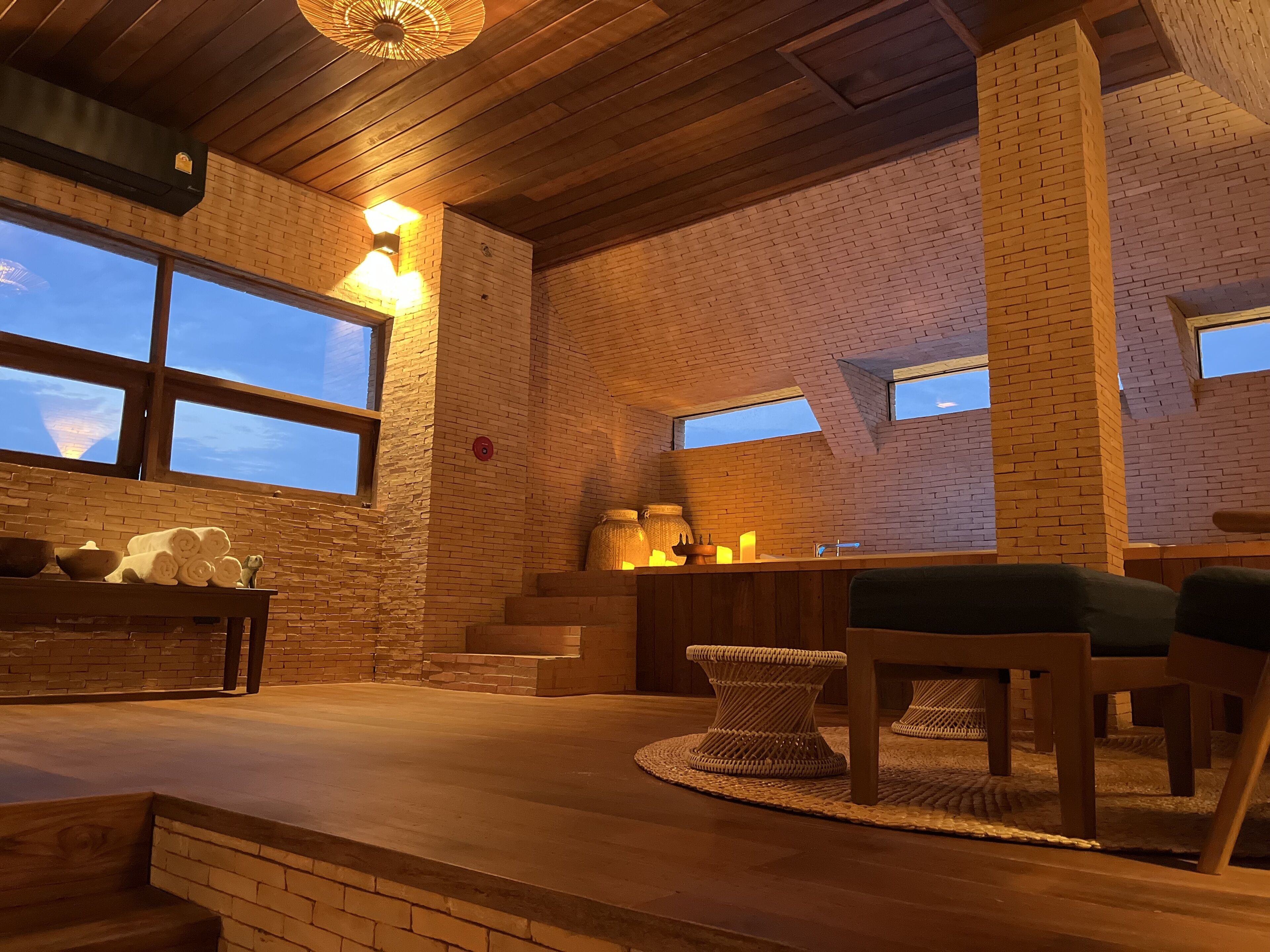 Un interior acogedor con pared de ladrillo, techo de madera y una mesa con taburete tejido.