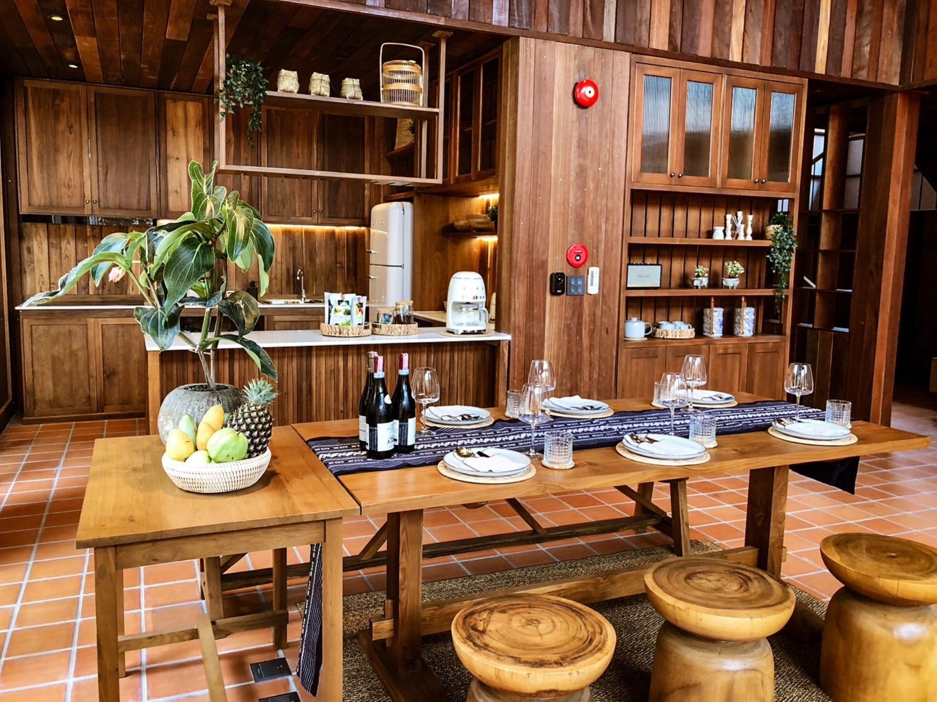 Interior de madeira com uma mesa de jantar posta para seis pessoas, rodeada por bancos de madeira.