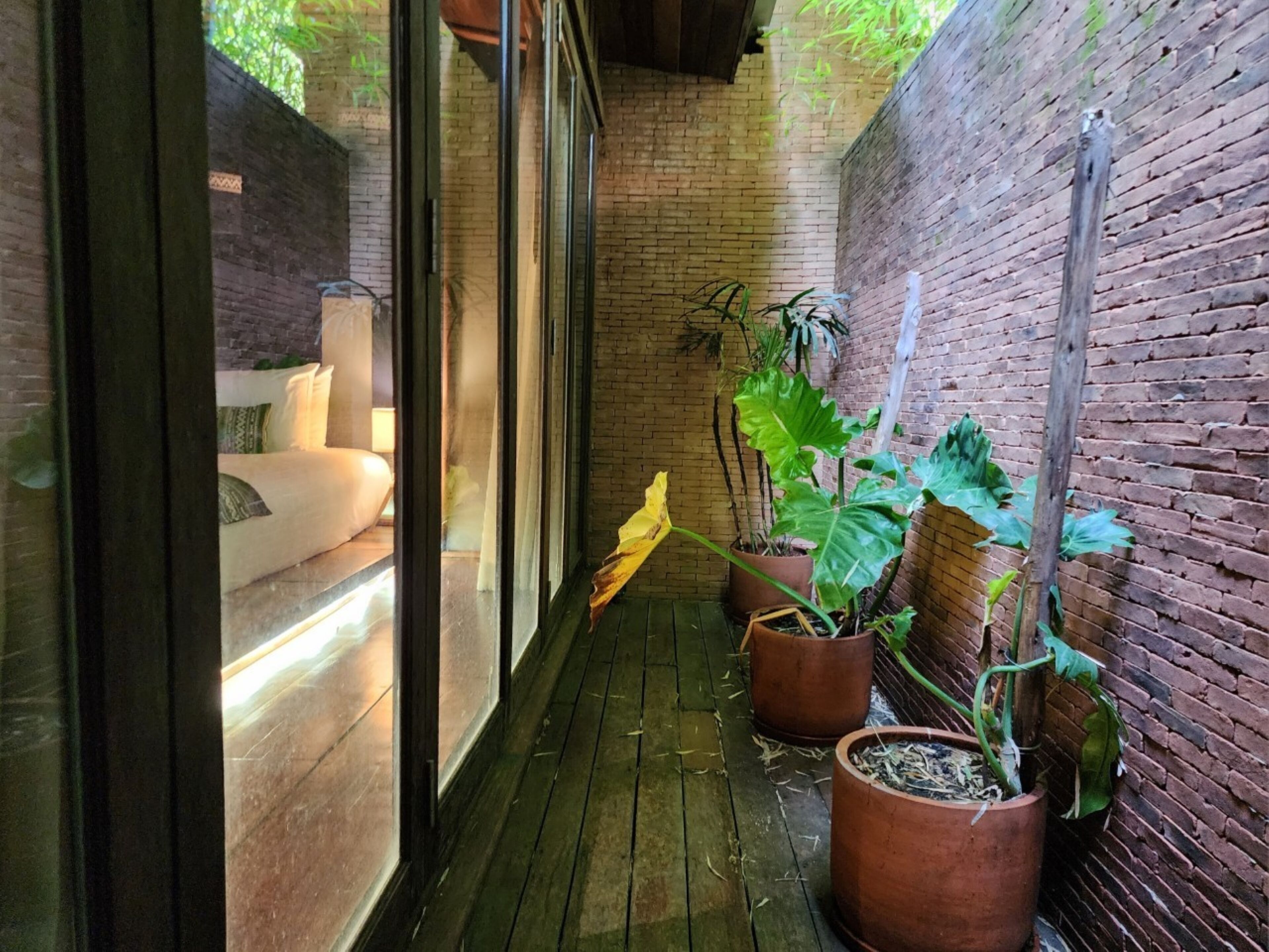 A narrow corridor with a wooden floor, brick walls, and potted plants.