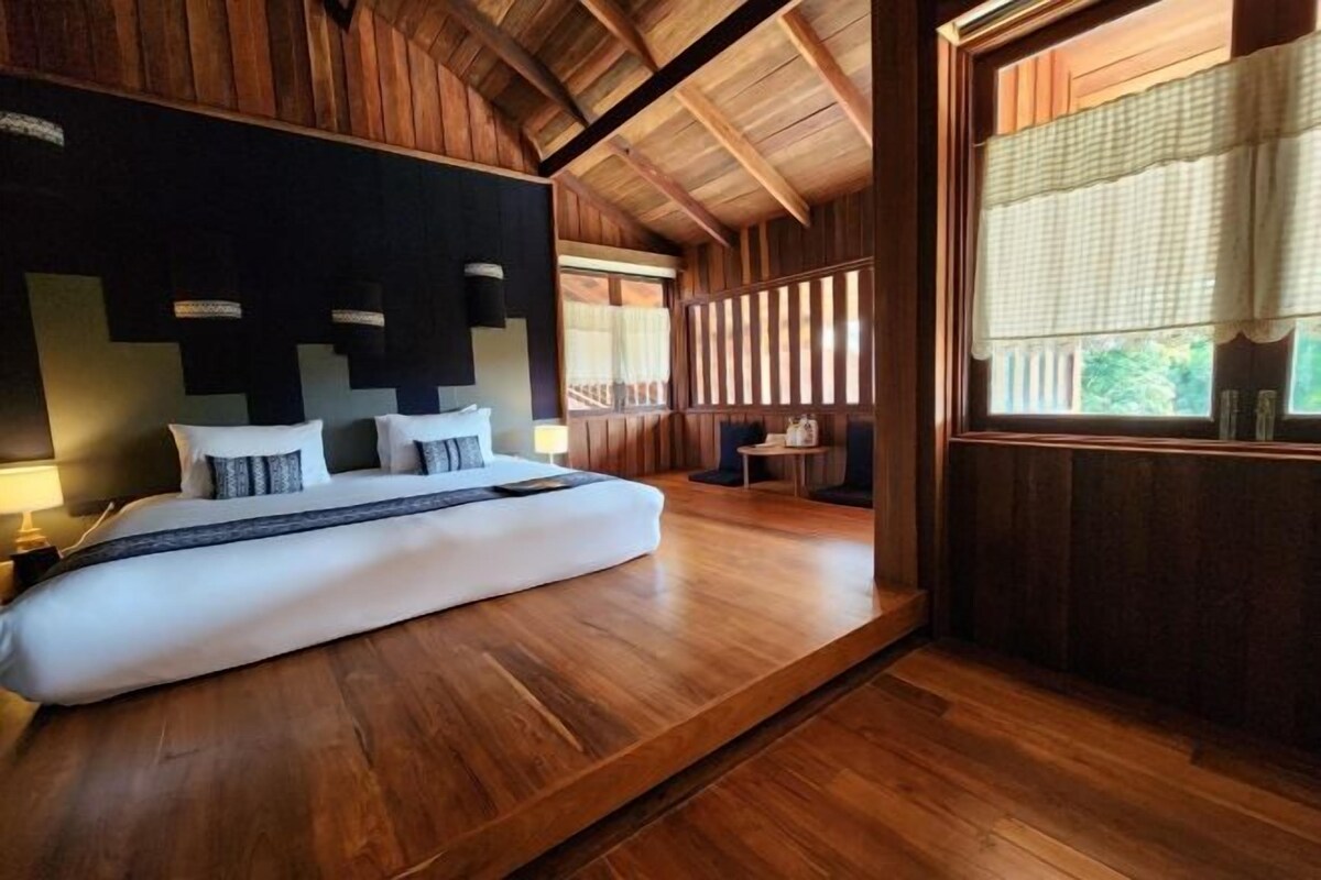 Une chambre à coucher moderne avec un grand lit, des poutres en bois au plafond et une vue sur l’extérieur par une fenêtre.