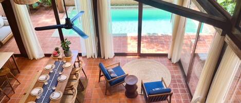 A spacious room with a large dining table set for six, a sofa, and a ceiling fan.