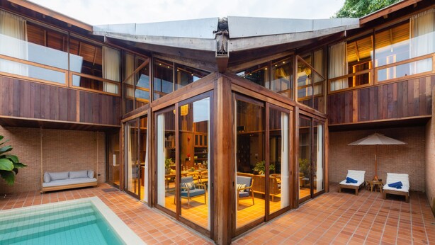 Ein modernes Haus mit Swimmingpool, Holzterrasse und Essbereich mit Gartenmöbeln.