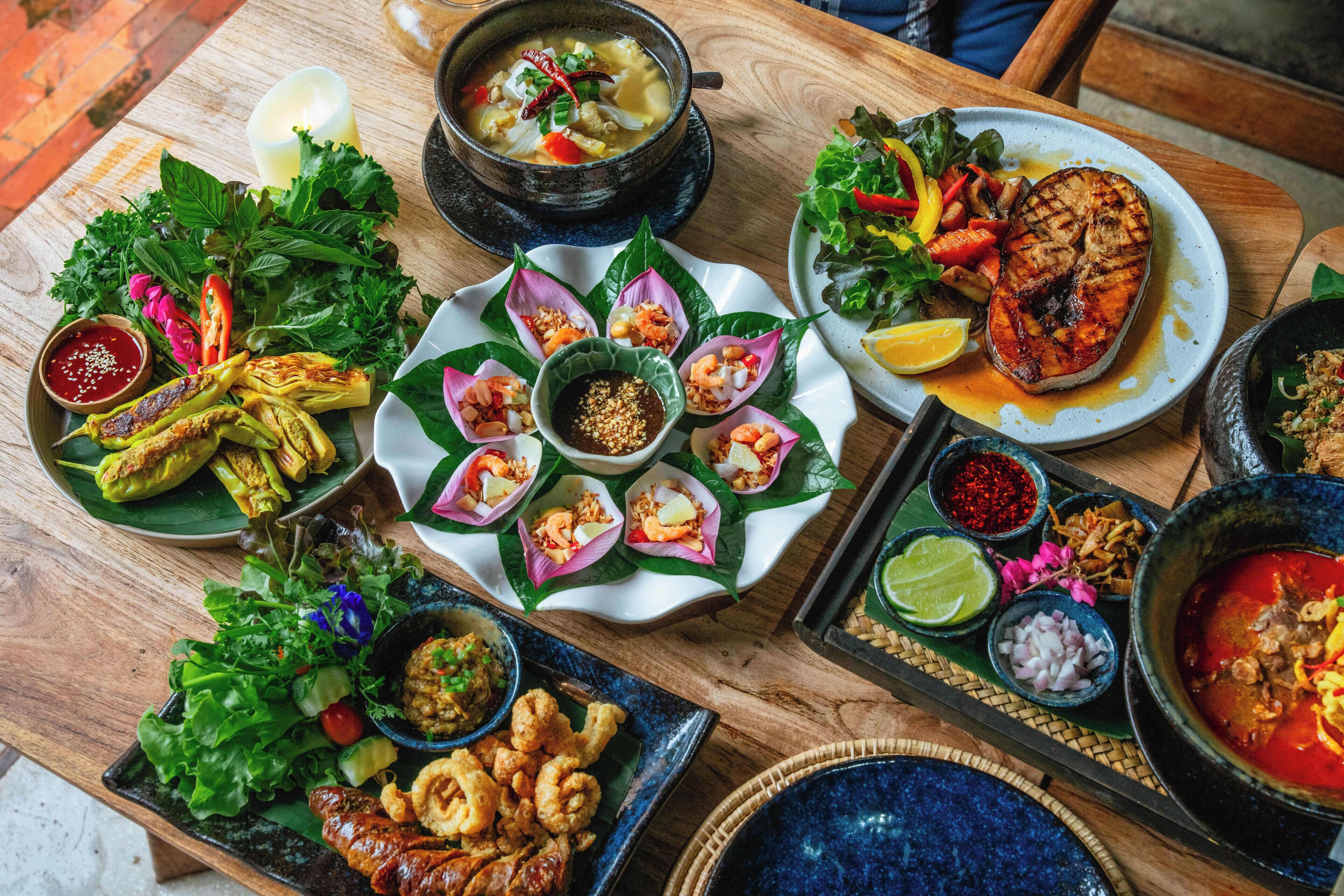 A variety of dishes on a wooden table, including grilled meat, seafood, and vegetables.