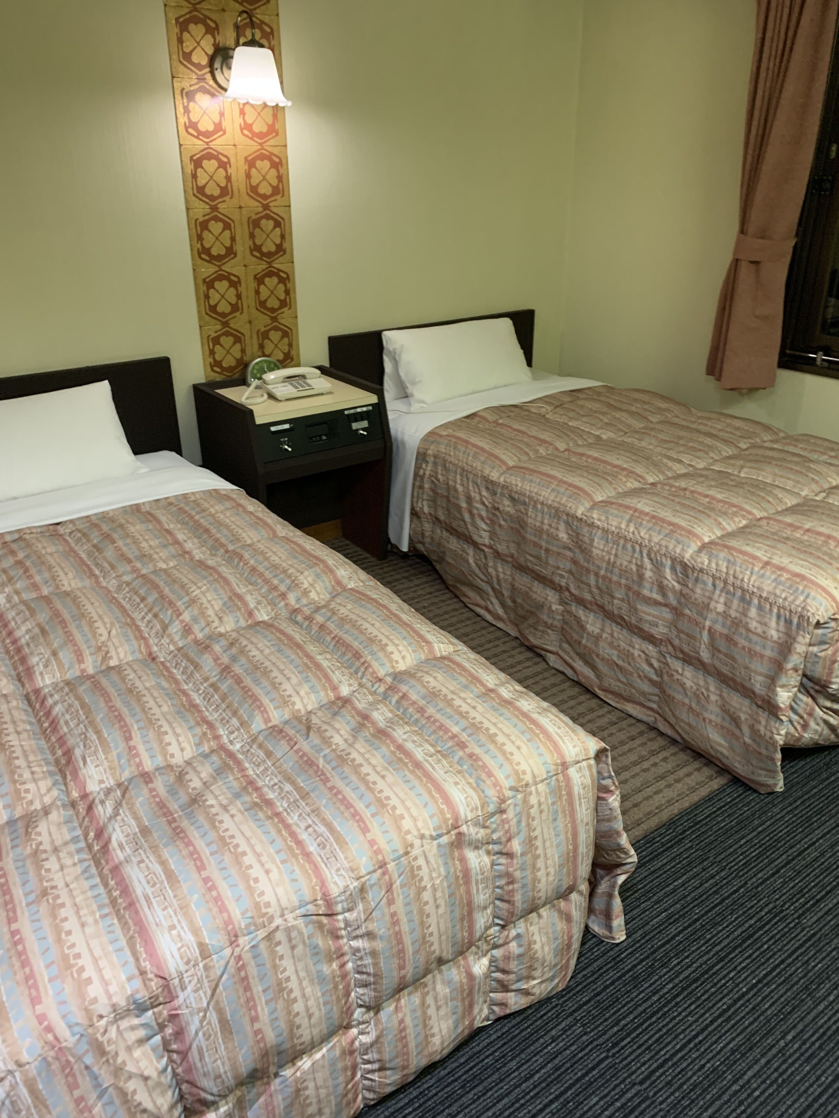Une chambre d’hôtel avec deux lits, une table de chevet avec un téléphone et une lampe fixée au mur.