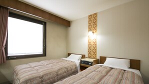 Habitación de hotel con dos camas, una ventana, una mesita de noche y una lámpara fijada a la pared.