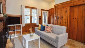 A cozy living room with a grey sofa, white coffee table, and wooden paneling. - Walk 1/10 Mile to Lecount Hollow Beach! (Wellfleet)