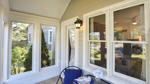 A covered patio with large windows, a table with a chair, and a hanging lantern. - Walk 1/10 Mile to Lecount Hollow Beach! (Wellfleet)