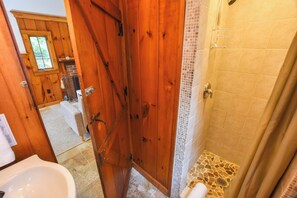 A wooden bathroom with a shower, a visible window, and a tiled floor.