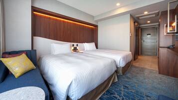 A hotel room with two beds, a sofa, a small table, and a bathroom visible through an open door.