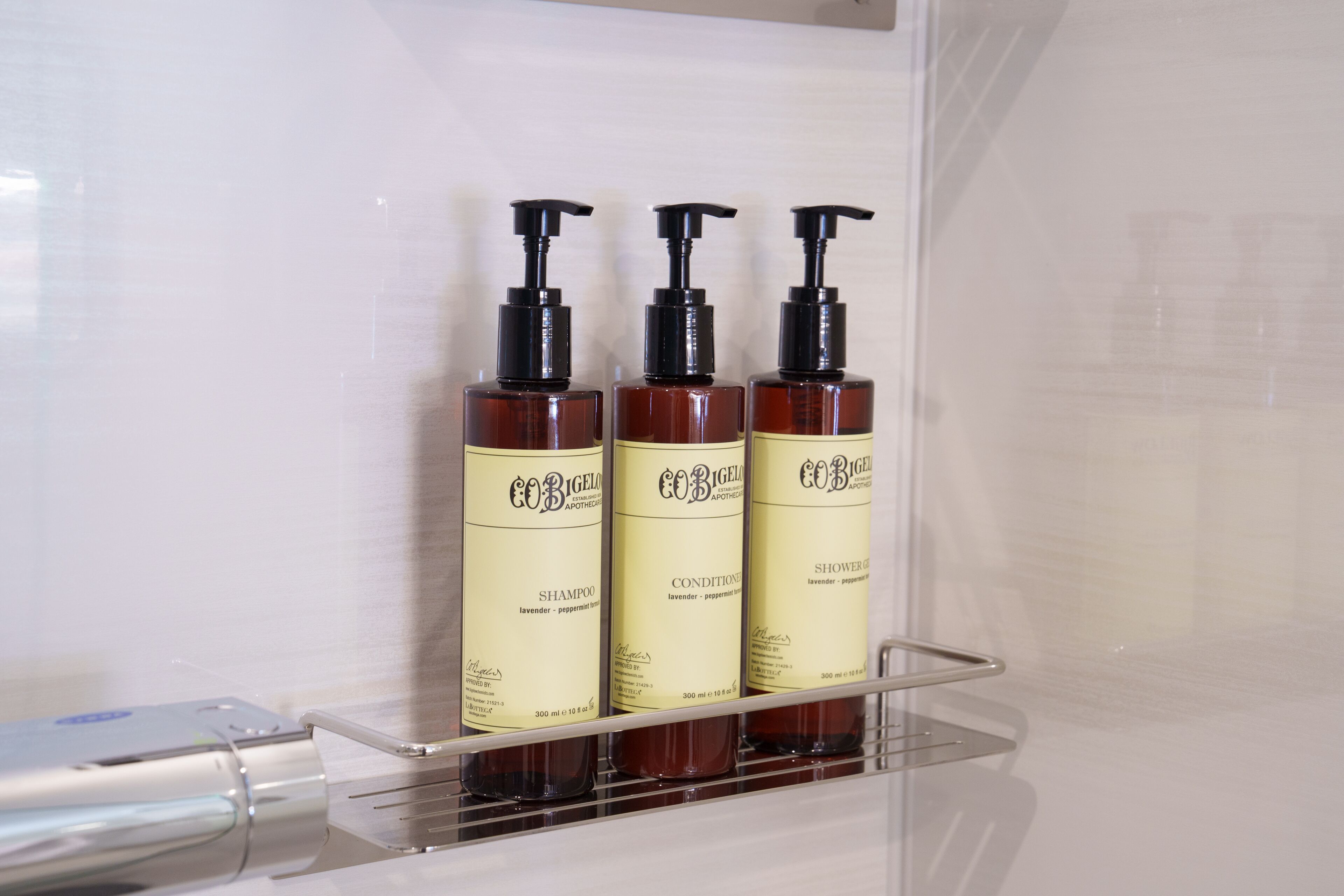 Tres botellas de champú y acondicionador sobre una repisa transparente en un baño.