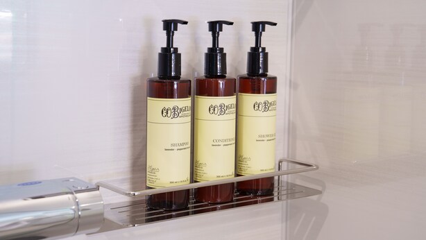 Trois bouteilles de shampoing et d’après-shampoing sont posées sur une étagère transparente dans une salle de bain.