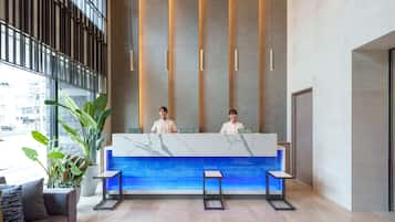 A reception desk with two staff members, a large potted plant, and a modern interior design.