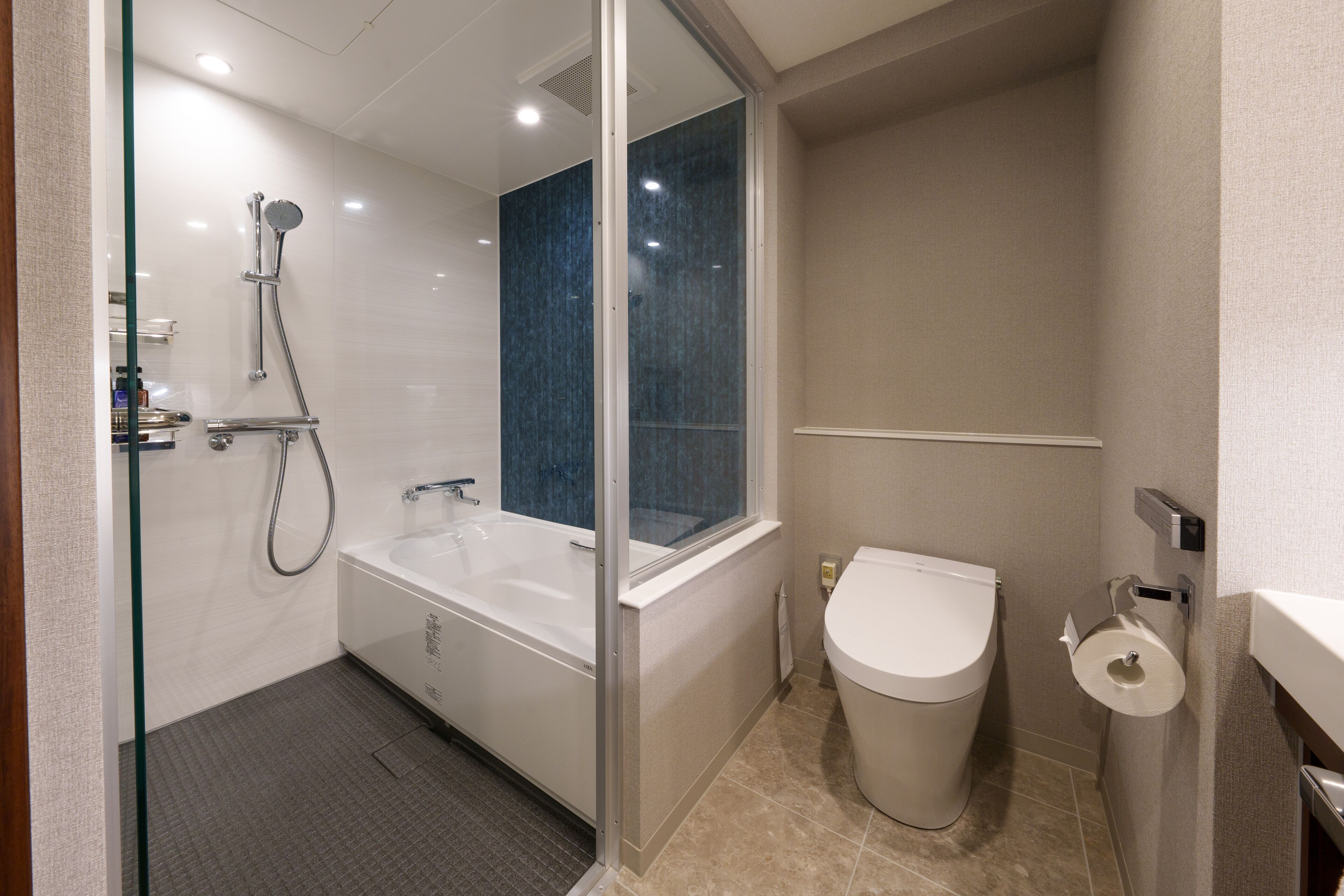 Une salle de bain moderne avec une douche à parois de verre, une baignoire blanche et des toilettes équipées d’un distributeur de serviettes en papier.