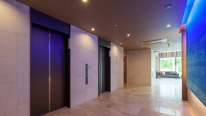 A modern hallway with elevators, a seating area, and a large window. - Hotel Grand Consort Naha (Naha)