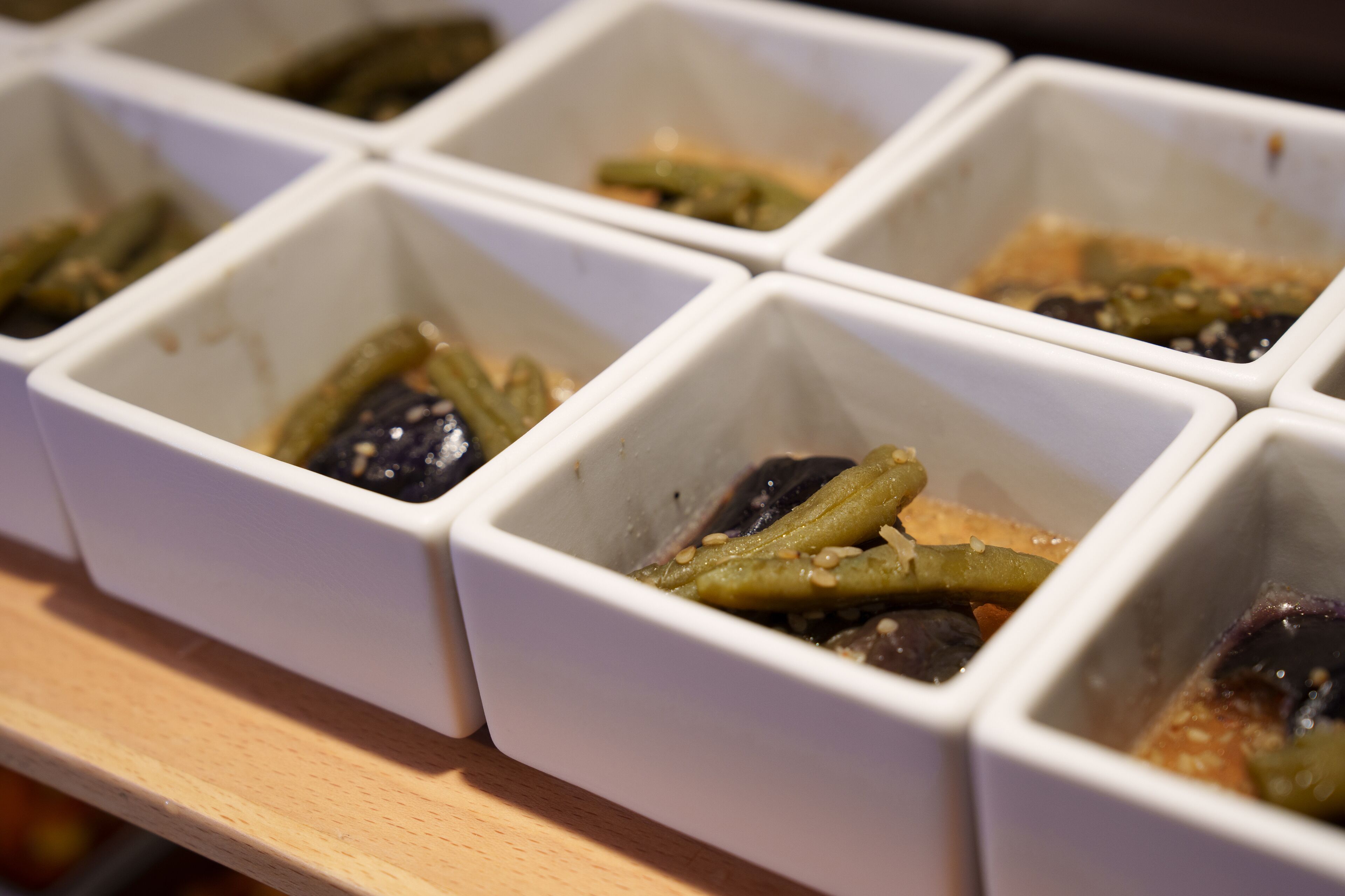 A row of white containers with various pickled vegetables.