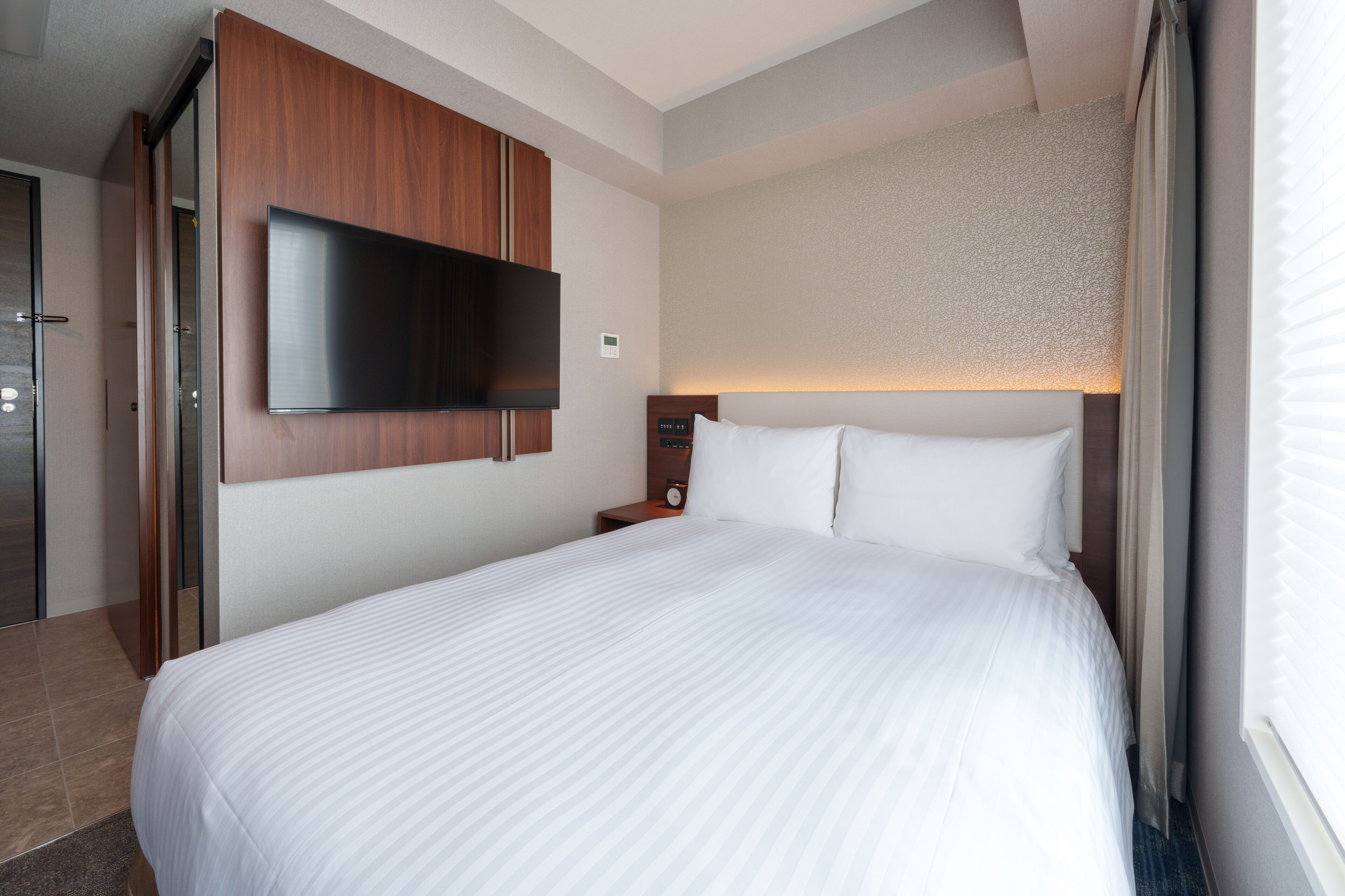 Ein Hotelzimmer mit einem großen Bett, einem flachbildfernseher an der Wand, einem Holz-Kopfteil und einem Nachttisch mit einer Uhr.
