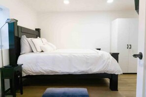 Ein Schlafzimmer mit einem Bett, einem Nachttisch, einem Kleiderschrank und einem Schreibtisch mit Lampe.