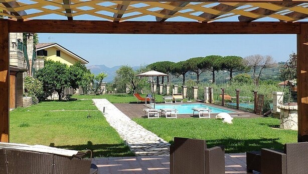 Een zwembadgedeelte met een pergola, ligbedden en een pad dat naar een huis leidt.