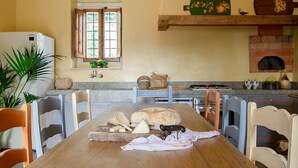 Une cuisine avec une table en bois, des chaises, une miche de pain, du fromage et un couteau.