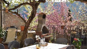 Un espace de restauration en plein air avec un four en pierre, des chaises en métal et une table dressée pour deux personnes.