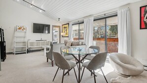 En moderne stue med et sofabord med glasplade, grå stole, en sofa og et fladskærms-tv ophængt på væggen.