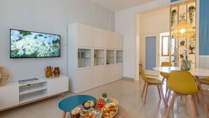Sala de estar moderna com televisão de tela plana, armários brancos, área de jantar com cadeiras amarelas e uma parede azul de destaque.
