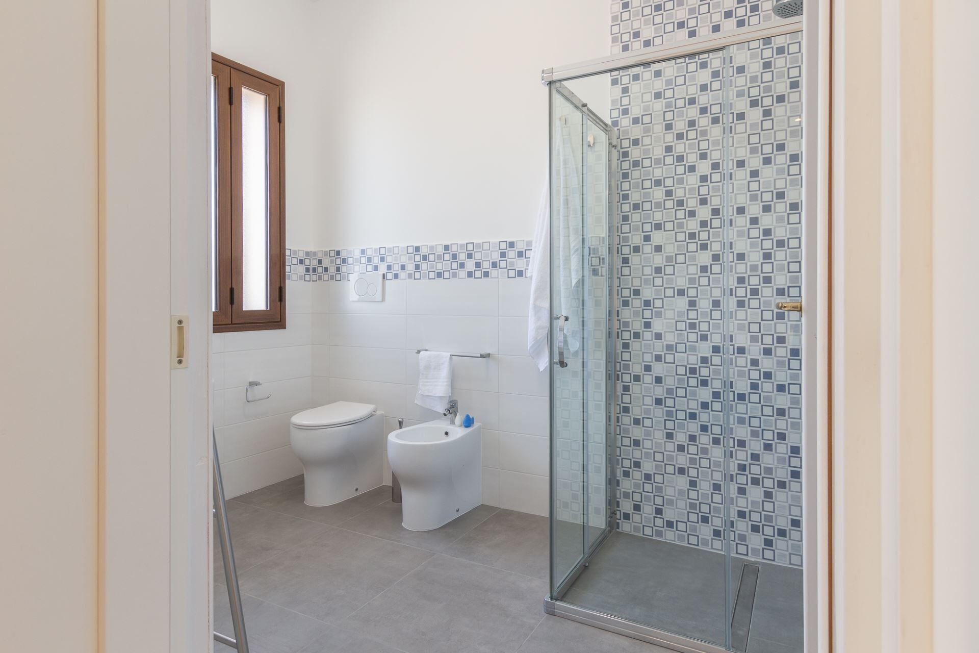 Ein Badezimmer mit zwei Toiletten, einer Duschkabine aus Glas und einer gefliesten Rückwand.