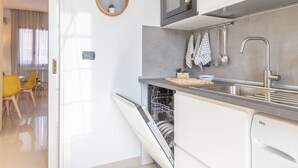 Cozinha moderna com máquina de lavar louça embutida, micro-ondas e pia. Duas cadeiras e uma mesa pequena na área de refeições adjacente.
