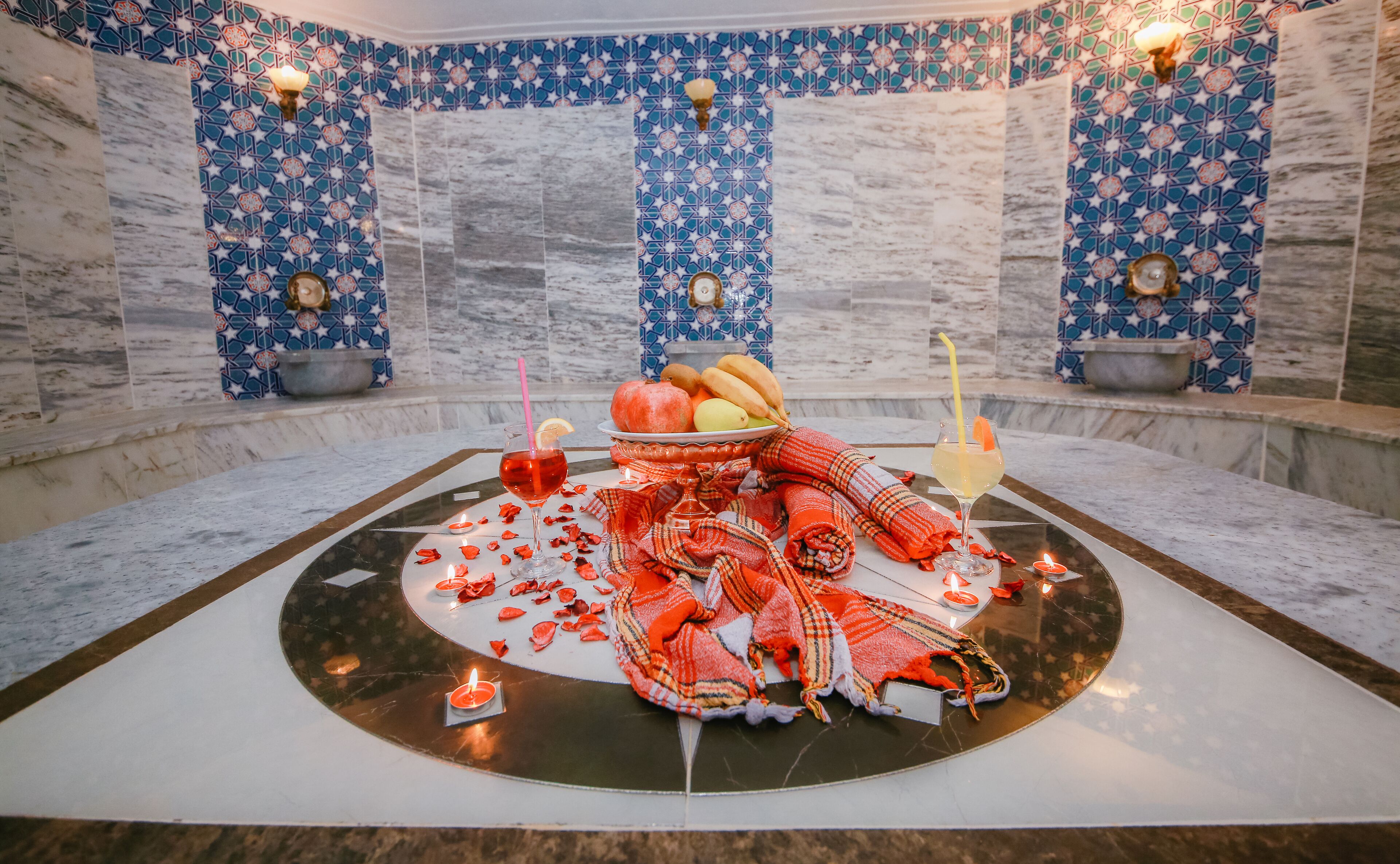 A room with a marble floor, a central table with a red cloth, candles, and a fruit bowl.