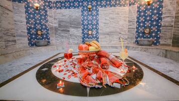 A room with a marble floor, a central table with a red cloth, candles, and a fruit bowl.