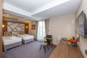 A hotel room with two beds, a dining table with a fruit bowl and flowers, and a chair. - Litros Hotel & Spa (Istanbul)