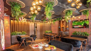 A restaurant with wooden tables, black cushioned chairs, hanging plants, and a TV mounted on the wall. - Litros Hotel & Spa (Istanbul)