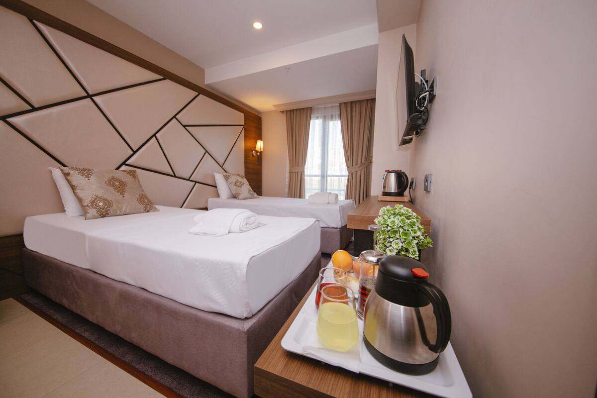 Une chambre d’hôtel avec un grand lit, un plus petit lit, un bureau avec une bouilloire et un plateau contenant des articles pour le petit-déjeuner.
