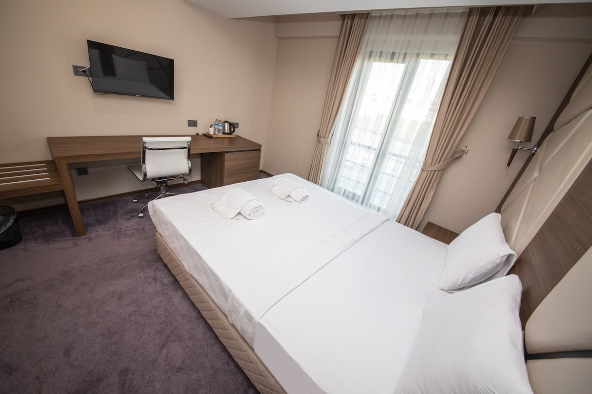 Une chambre d’hôtel équipée d’un lit, d’un bureau, d’une chaise, d’une télévision et d’une fenêtre avec des rideaux.