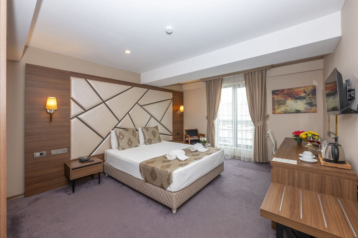 Une chambre d’hôtel avec un grand lit, des tables de chevet, un bureau avec une chaise, une télévision et une fenêtre avec des rideaux.
