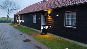 Un bâtiment en bois avec un toit recouvert de tuiles, deux fenêtres visibles et une allée pavée.