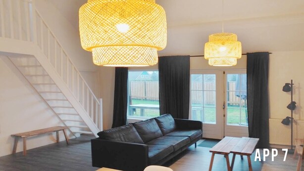 Un salon moderne avec un canapé en cuir noir, un banc en bois et deux grandes suspensions en fibres tressées.