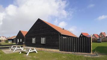 Ein schwarzes Holzgebäude mit rotem Dach, umgeben von ähnlichen Gebäuden, und ein Picknicktisch im Vordergrund.