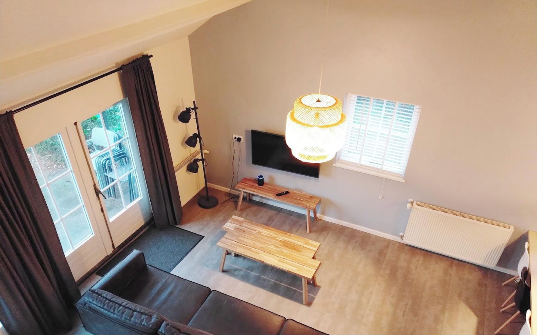 A modern living room with a sofa, a wooden bench, a floor lamp, and a TV mounted on the wall.