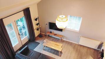 A modern living room with a sofa, a wooden bench, a floor lamp, and a TV mounted on the wall.