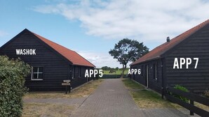 A rural setting with two black wooden buildings labeled 'WASHOK' and 'APP 7'. A paved path leads through the buildings.
