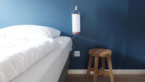 A bedroom with a bed, a wooden stool, and a white hanging lamp on a blue wall.